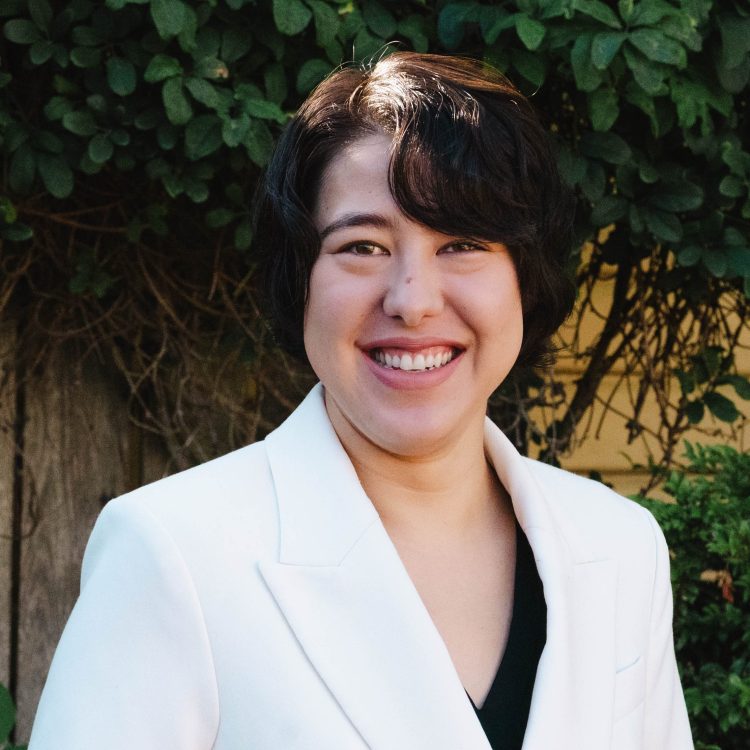 Lillian Powers. An Asian American woman with brown hair. She is wearing a white blazer over a black shirt.