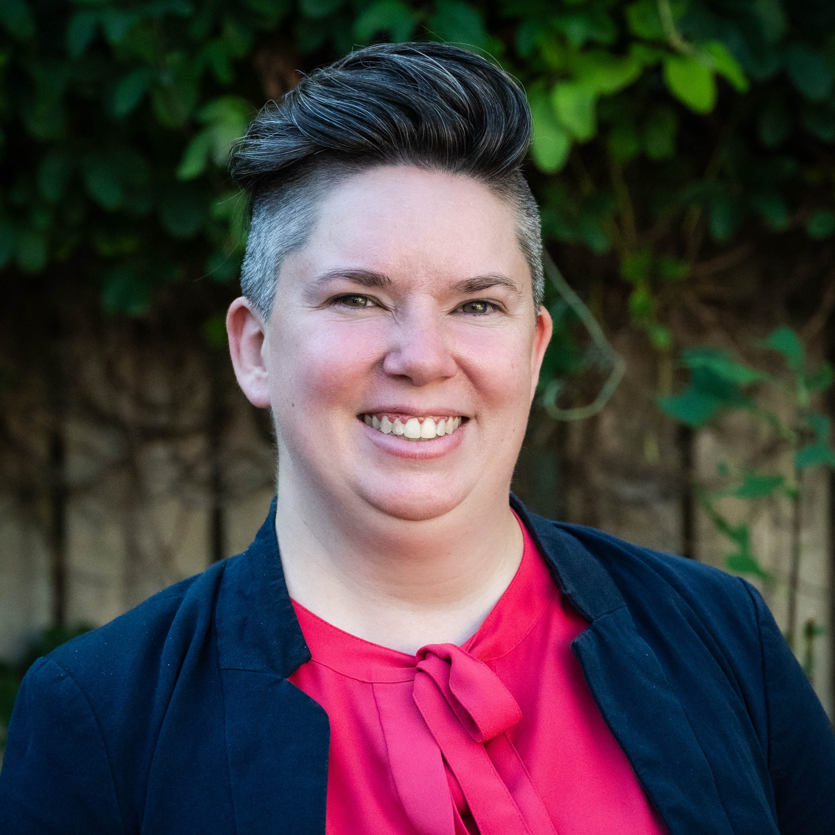 Navarra Carr. A white woman with black and grey hair. She is wearing a blue coat over a red shirt.